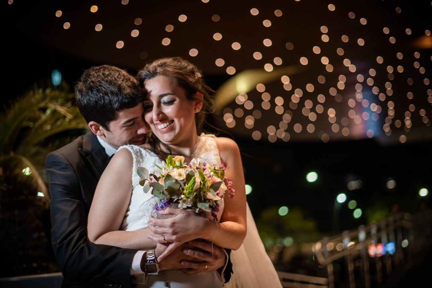 Novios abrazados de noche con luces de fondo — Proyecto Confite